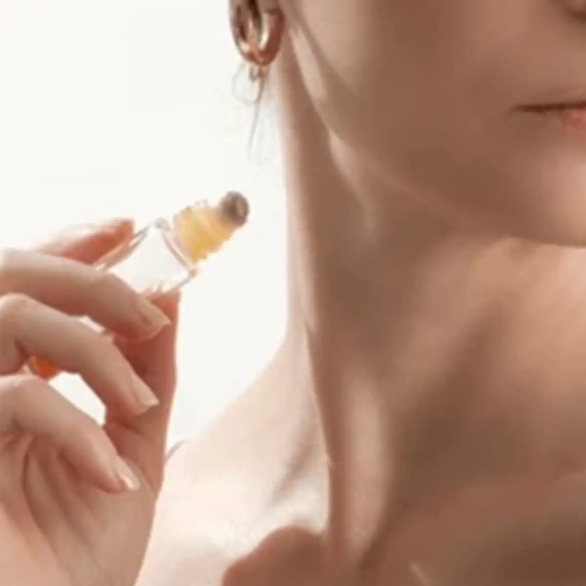 A clear glass rollerball perfume bottle with a golden cap and amber-colored liquid inside.