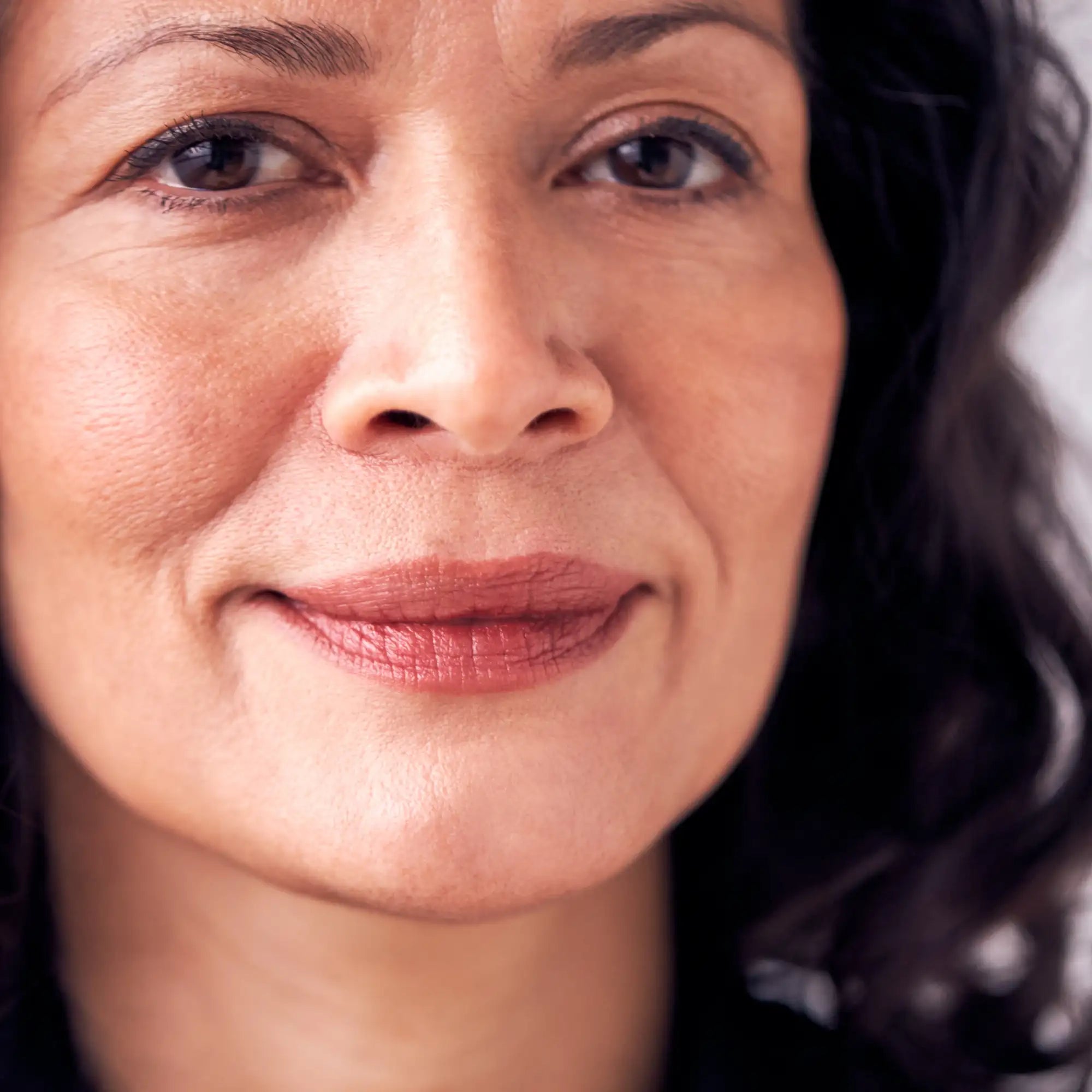 A close-up portrait of a woman with warm brown eyes and dark, wavy hair.
