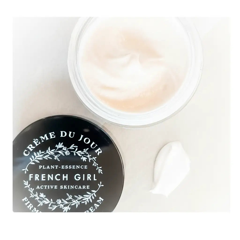 A sleek black lid with white botanical lettering and a clear glass jar containing creamy, off-white skincare cream.